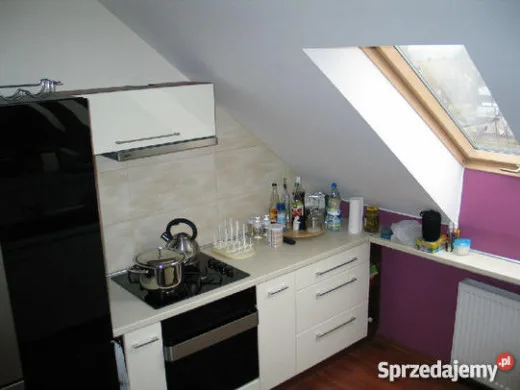 Kuchnia utrzymana w bieli i fiolecie z oknem w strefie roboczej